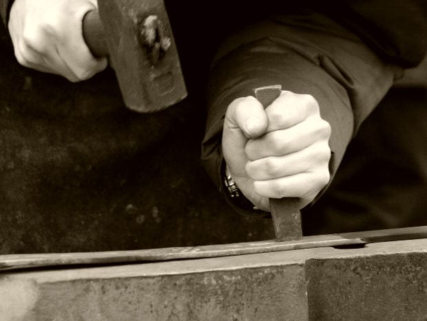 Close-up of worker’s hands using a hammer and chisel on metal, symbolizing occupational asbestos exposure at industrial worksites.