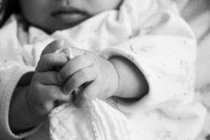 Black and white photo of an infant’s hands clutching a blanket, symbolizing child safety concerns tied to defective car seat recalls.