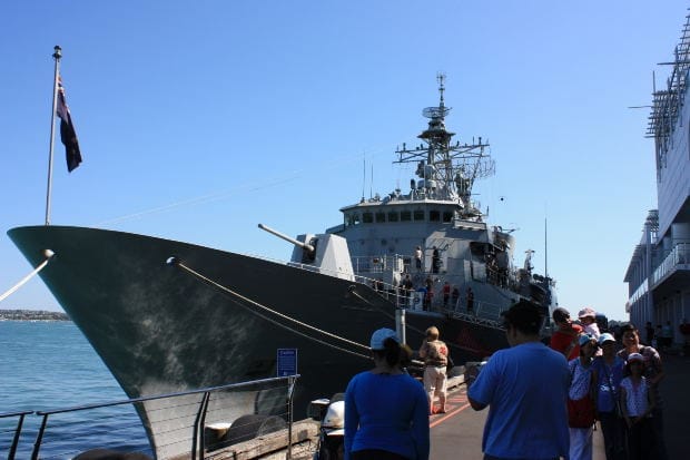 Large Navy ship docked at port with visitors walking nearby, representing asbestos exposure risks faced by veterans aboard naval vessels.