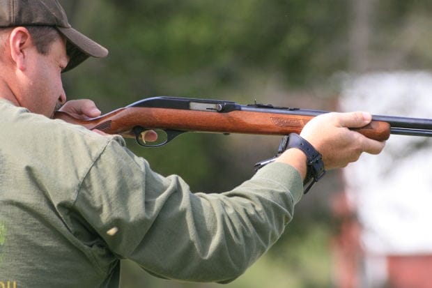 A hunter in a green shirt aiming a rifle outdoors, representing treestand hunting accident litigation in Bradley v. Ameristep, Inc.