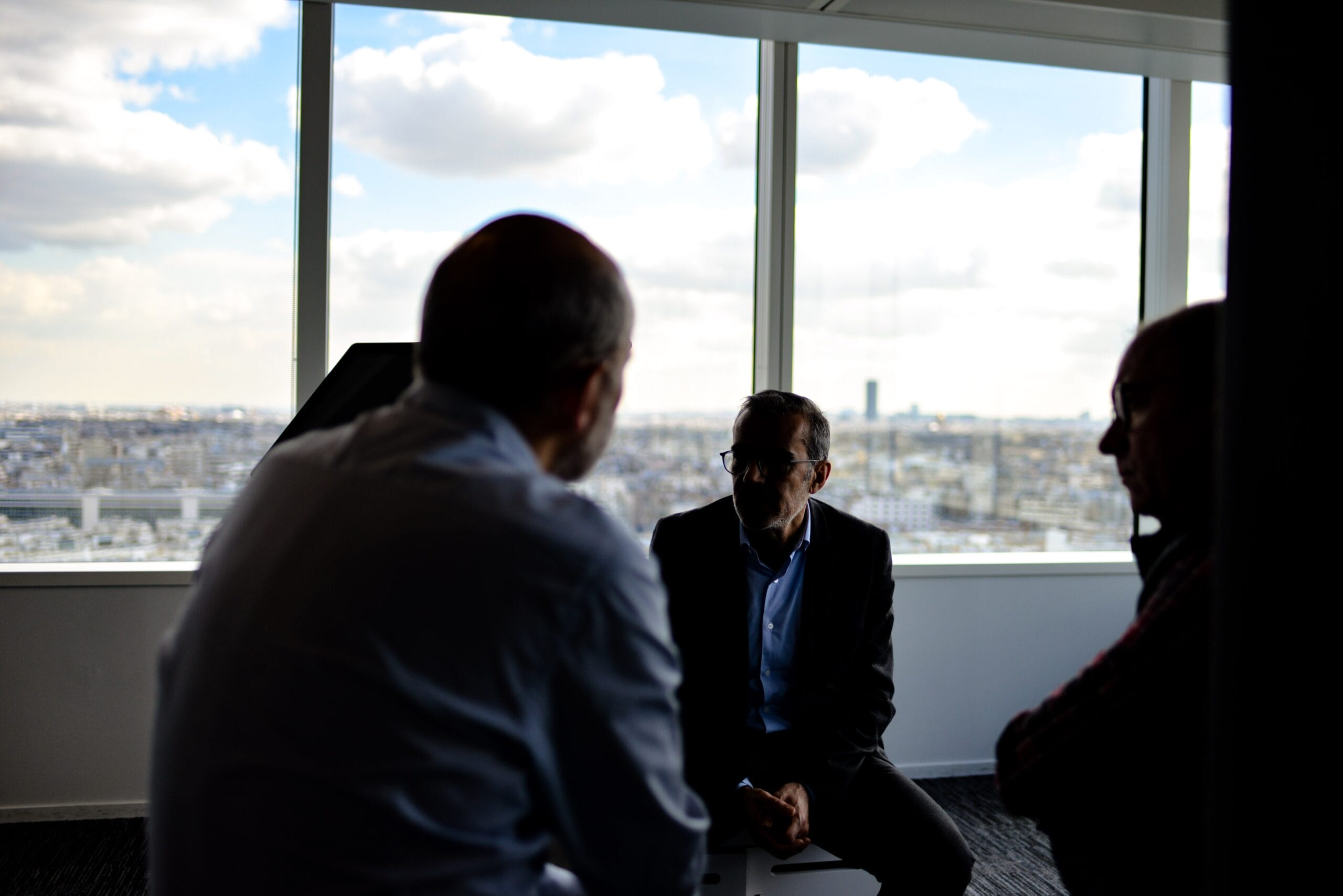 Three men in a dimly lit office with a city skyline view, engaged in a serious discussion, symbolizing the private nature of wrongful death case consultations in Florida.