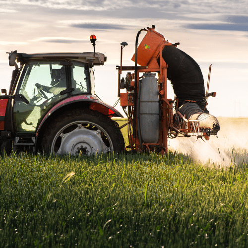 Tractor equipped with a sprayer applying herbicide to a green crop field, representing paraquat exposure risks.