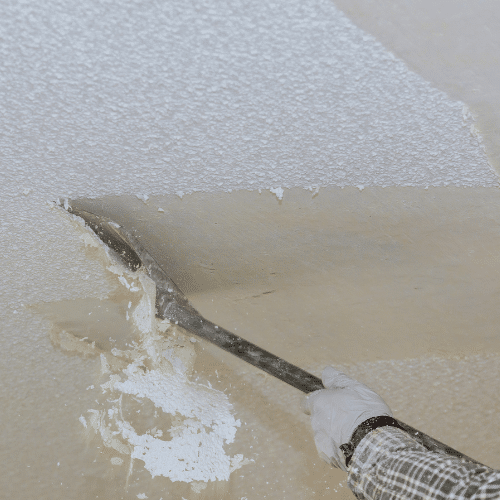 Close-up of a worker scraping a textured popcorn ceiling, a process that may release asbestos fibers if the material contains asbestos.