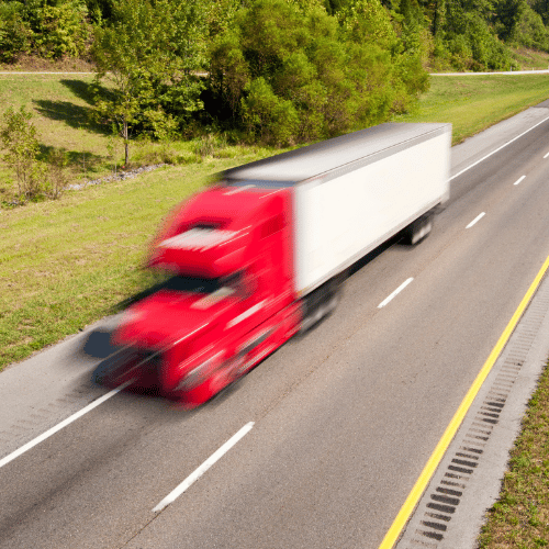 Blurred red semi-truck traveling at high speed on a highway, representing the urgency and potential dangers of 18-wheeler accidents.