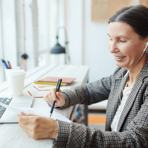 Professional woman in a plaid blazer smiling while reviewing documents at her desk with a laptop, pen, and coffee cup, symbolizing the expertise and strategic thinking a commercial litigator can provide.