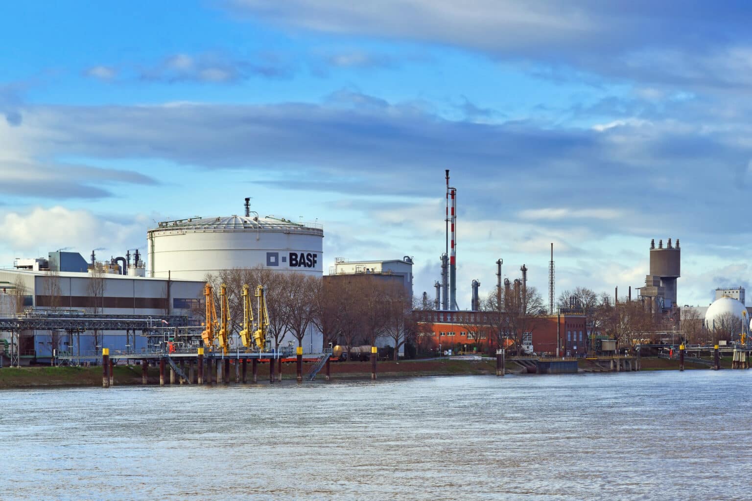 BASF industrial facility with storage tanks, smokestacks, and dockside equipment along a river, representing PFAS contamination and related legal settlements