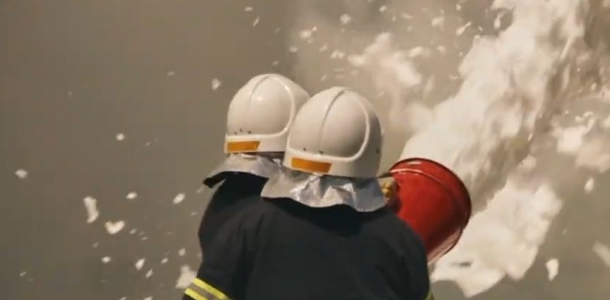 Two firefighters in protective gear spraying AFFF firefighting foam during an emergency, illustrating potential PFAS exposure risks.